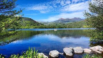 Un lac paisible avec un bateau, entouré d’une végétation luxuriante et avec des montagnes en arrière-plan.