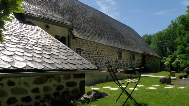 Un bâtiment en pierre avec un toit en pente, une pelouse verdoyante et une chaise pliante.