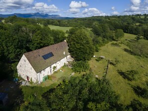 A stone house with a sloped roof and a solar panel, surrounded by lush greenery and hills in the background. - Holiday Home 'Chambres D'hôtes Et Gîte Du Domaine' with Mountain View and Wi-Fi (Bagnols)