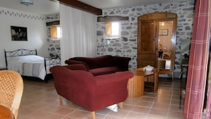 Une pièce avec un lit, un canapé rouge, une armoire en bois et un mur en pierre.