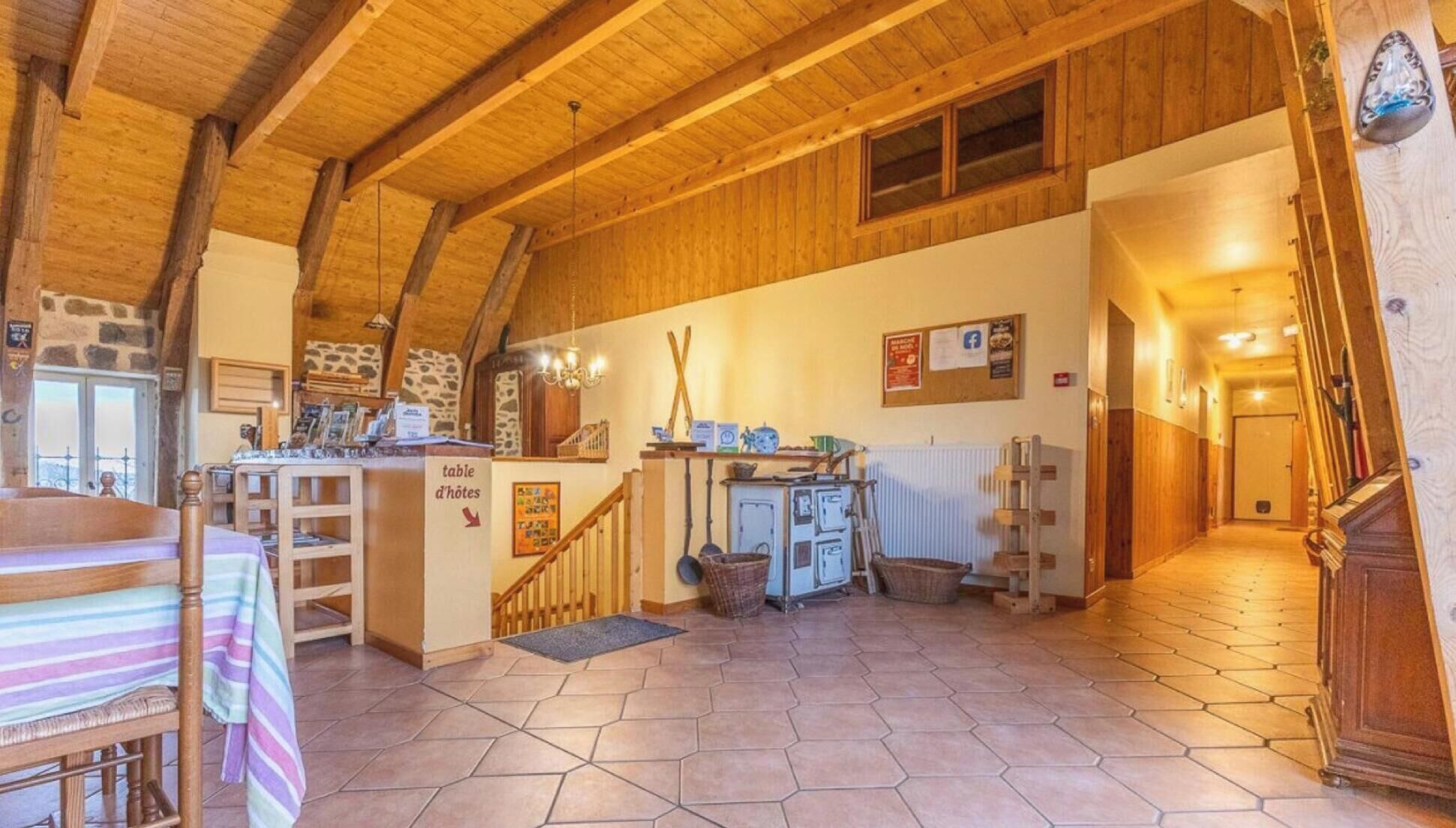 Un intérieur rustique avec un escalier en bois, un coin repas comprenant une table et des chaises, et une cuisine équipée de placards et d’un radiateur.