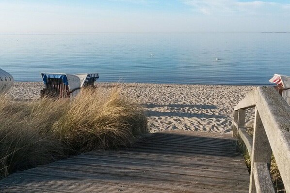 A wooden boardwalk leading to beach chairs on a sandy shore.