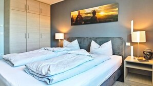 Ein Doppelbett mit weißer Bettwäsche, einem grauen Kopfteil und einem Wandbild, das einen Sonnenuntergang zeigt.
