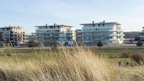 Ein Wohngebiet mit modernen Mehrgeschossgebäuden, einem grünen Feld im Vordergrund und einem wolkenlosen Himmel.