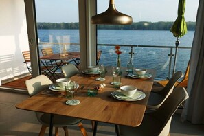 A dining area with a table set for four, overlooking a body of water. - House Kiki, Apartment 2 "Waikiki" (Heiligenhafen)