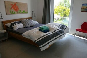 A bedroom with a bed, pillows, a nightstand, a red chair, and artwork on the walls. - House Kiki, Apartment 2 "Waikiki" (Heiligenhafen)