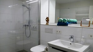 Et stilfuldt badeværelse med glasvæg omkring brusebad, et hvidt toilet og en vask med spejl over.