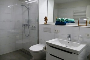 A modern bathroom with a glass shower enclosure, a white toilet, and a sink with a mirror above it. - House Kiki, Apartment 2 "Waikiki" (Heiligenhafen)