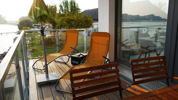 En balkon med to liggestole og et bord, med udsigt over vand og et bjerg.