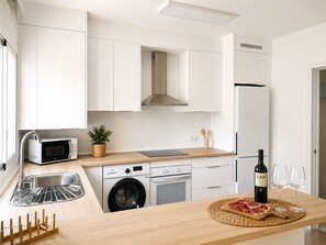 Eine moderne Küche mit Mikrowelle, Waschmaschine, Backofen und einer Weinflasche auf der Arbeitsfläche.
