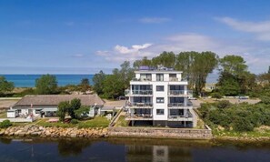 A multi-story building with balconies, situated by a body of water, with a clear view of the sea in the background. - Holiday apartment with 2 bedrooms (Heiligenhafen)