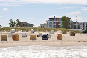 A beach with beach chairs and a building in the background. - Holiday apartment with 1 bedroom (Heiligenhafen)
