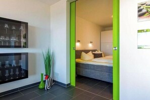 Une chambre moderne avec un lit, un téléviseur fixé au mur et une porte verte donnant sur une autre pièce.