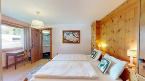 Quarto com duas camas, guarda-roupa de madeira, escrivaninha e banheiro visível por uma porta aberta.