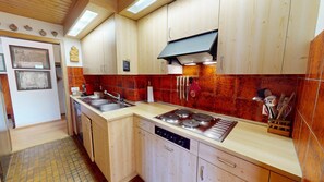 A kitchen with wooden cabinets, a gas stove, and a sink. - Apartment house on the hillside of Celerina. (Celerina/Schlarigna)