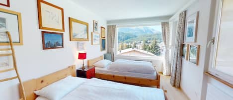 Une chambre avec deux lits, une fenêtre donnant sur la montagne et plusieurs tableaux encadrés accrochés au mur.