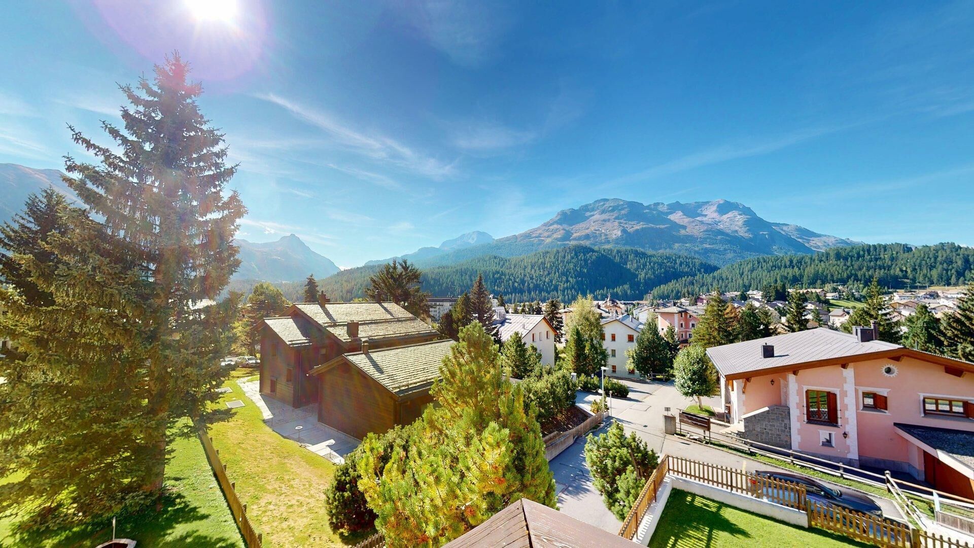 A residential area with houses, a large tree, and mountains in the background.