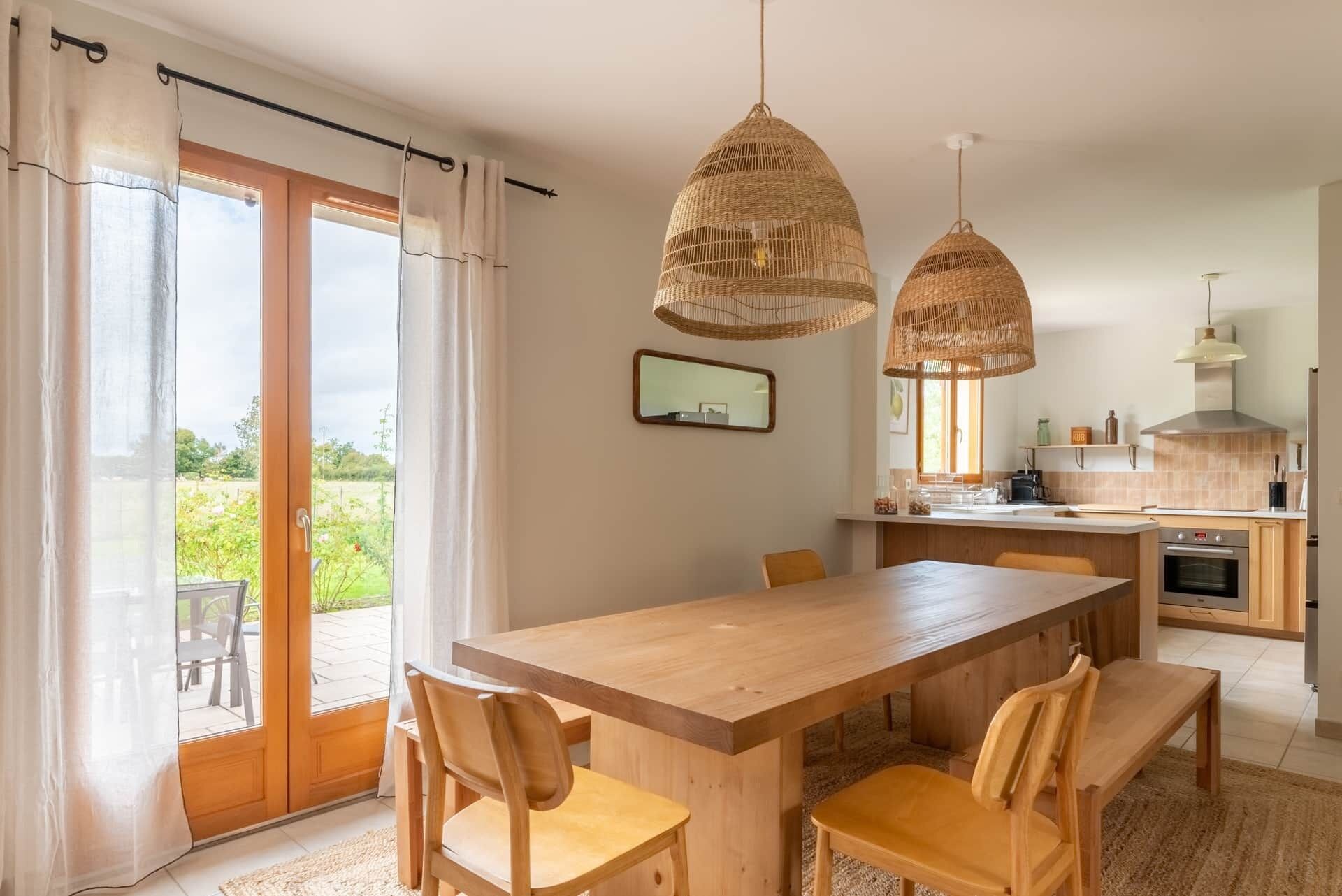 A dining area with a wooden table and chairs, a kitchen in the background, and a sliding glass door leading to an outdoor area.