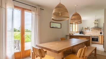 A dining area with a wooden table and chairs, a kitchen in the background, and a sliding glass door leading to an outdoor area.