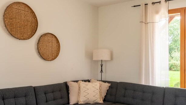 Een moderne woonkamer met een grijze modulaire bank, een ronde salontafel en twee geweven wanddecoraties.