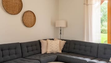 Un salon moderne avec un canapé d’angle gris, une table basse ronde et deux éléments décoratifs muraux en fibres tressées.