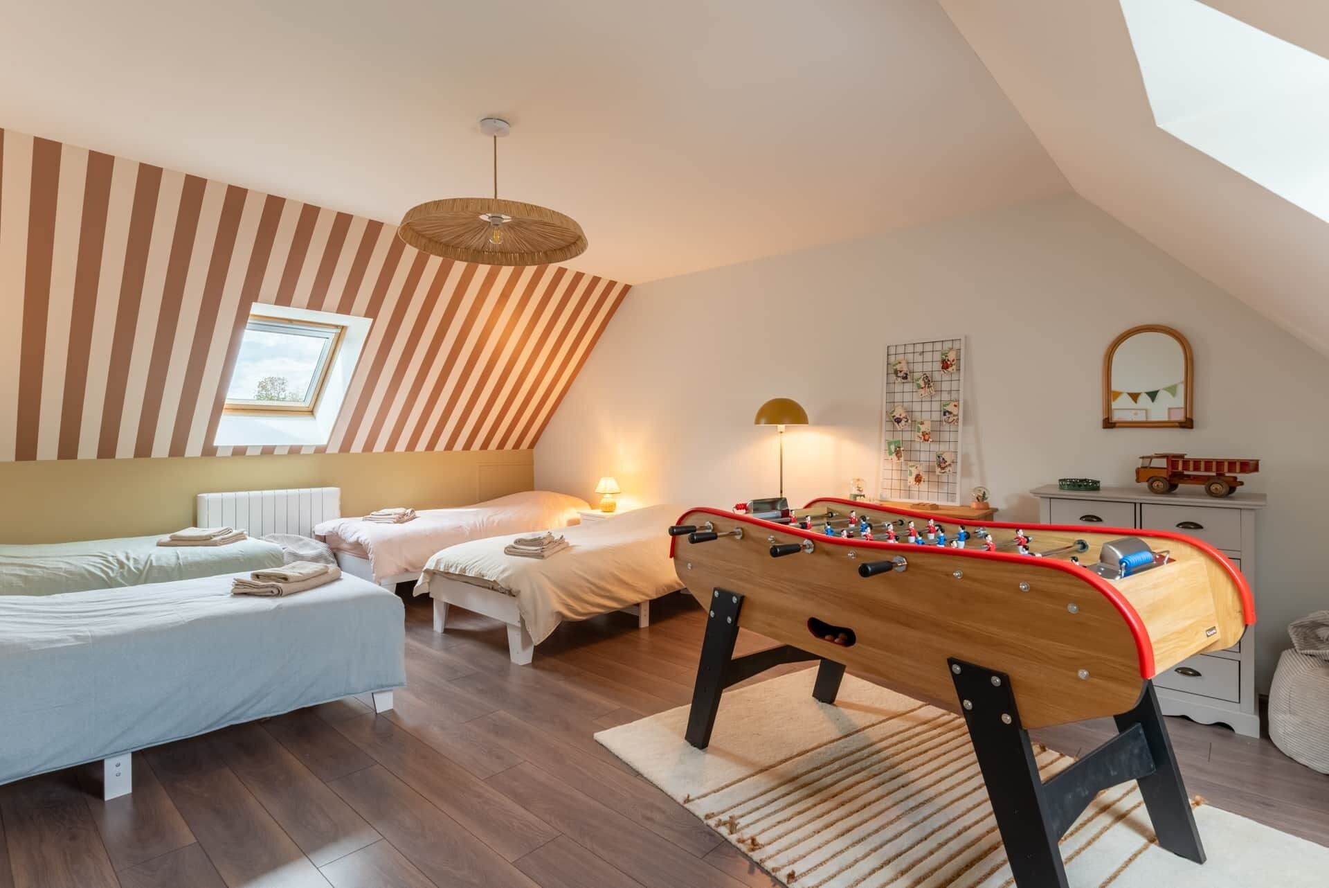 Une chambre confortable avec deux lits, un baby-foot et un plafond en pente avec une fenêtre.
