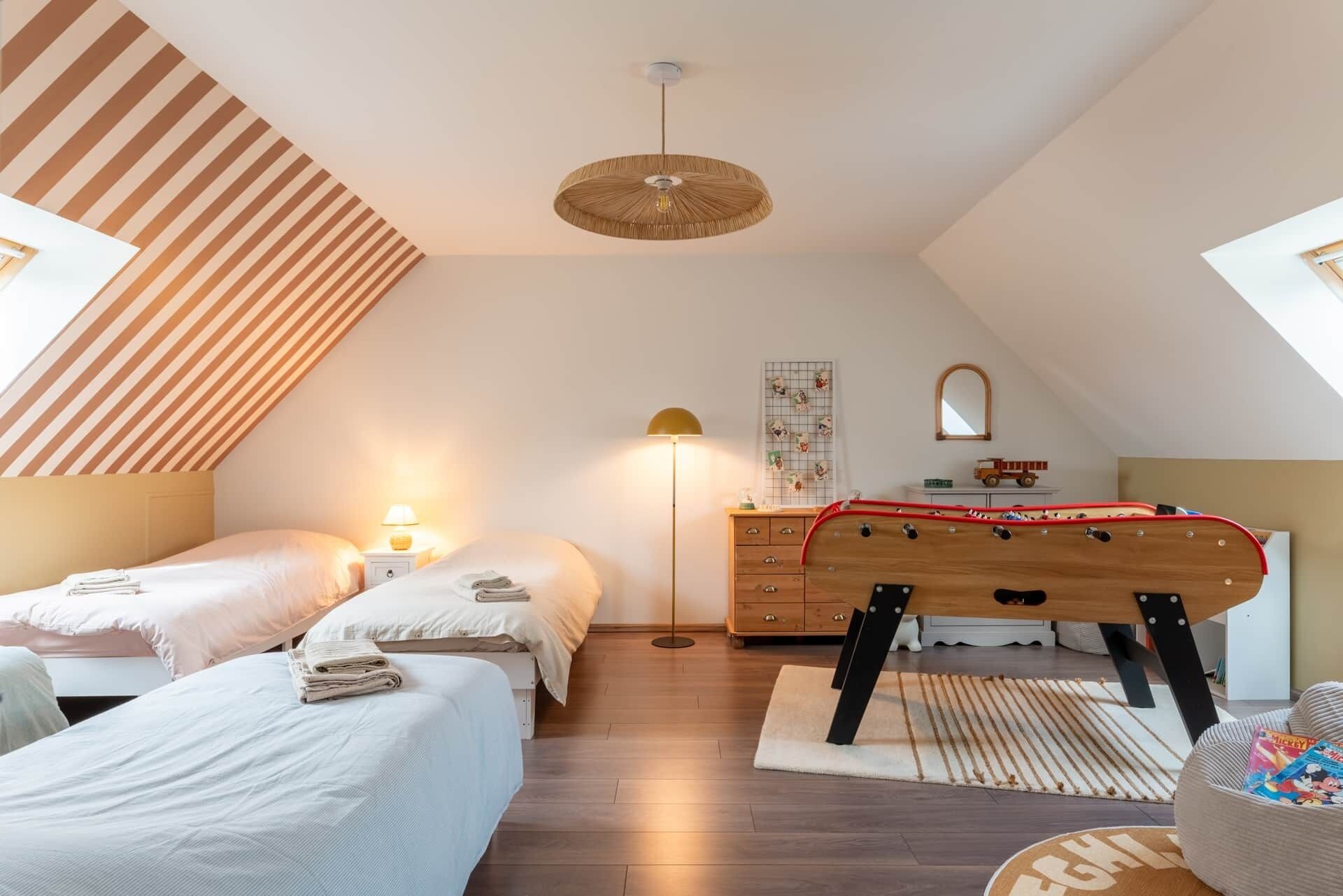 Une chambre avec deux lits, une commode en bois, une lampe sur pied et un ventilateur de plafond.