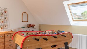 Een tafelvoetbaltafel in een kamer met een schuine plafond, een raam met uitzicht en een wandrek met foto's.