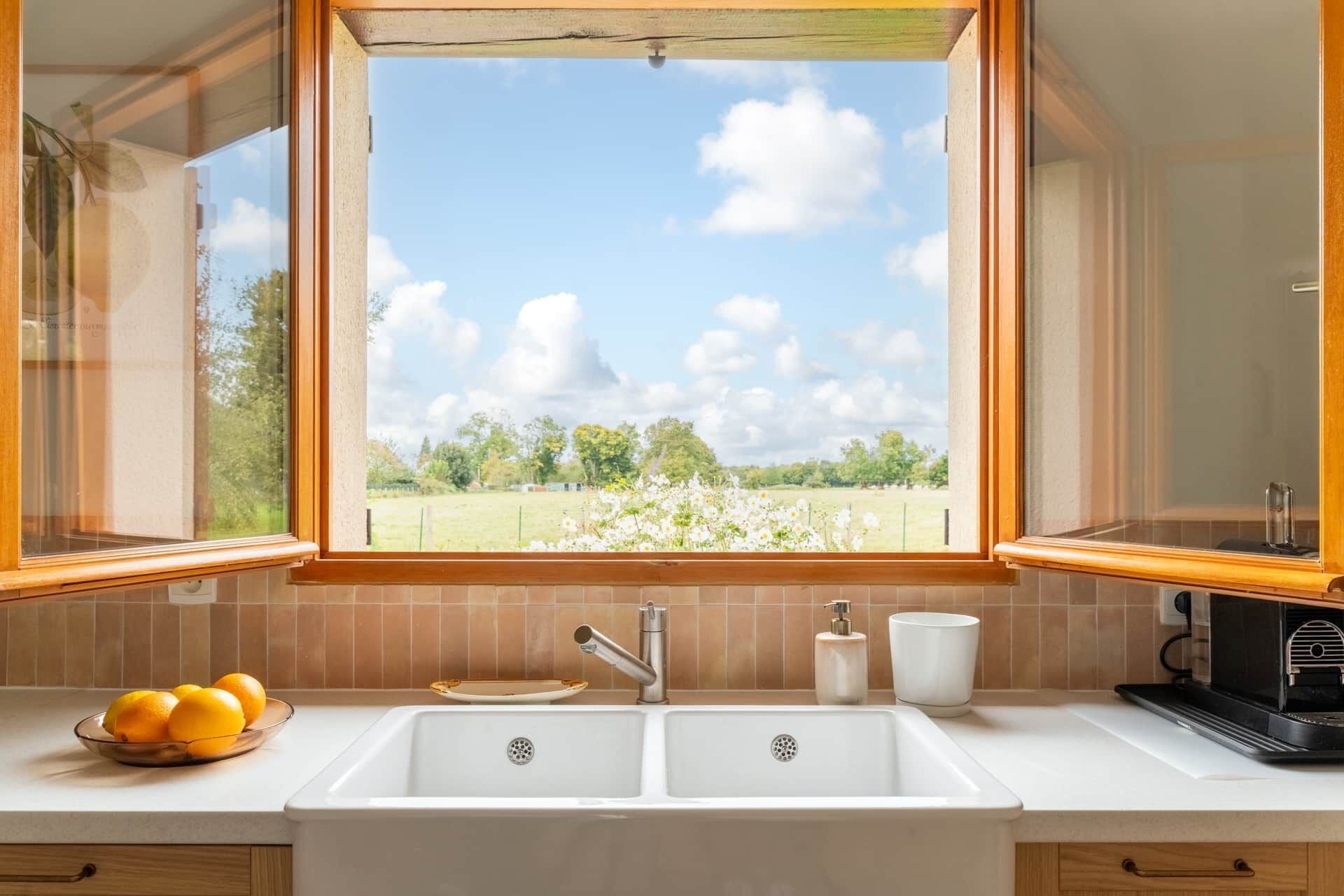 Eine Küche mit einem großen Fenster, einem Spülbecken und einer Schüssel Orangen auf der Arbeitsfläche.