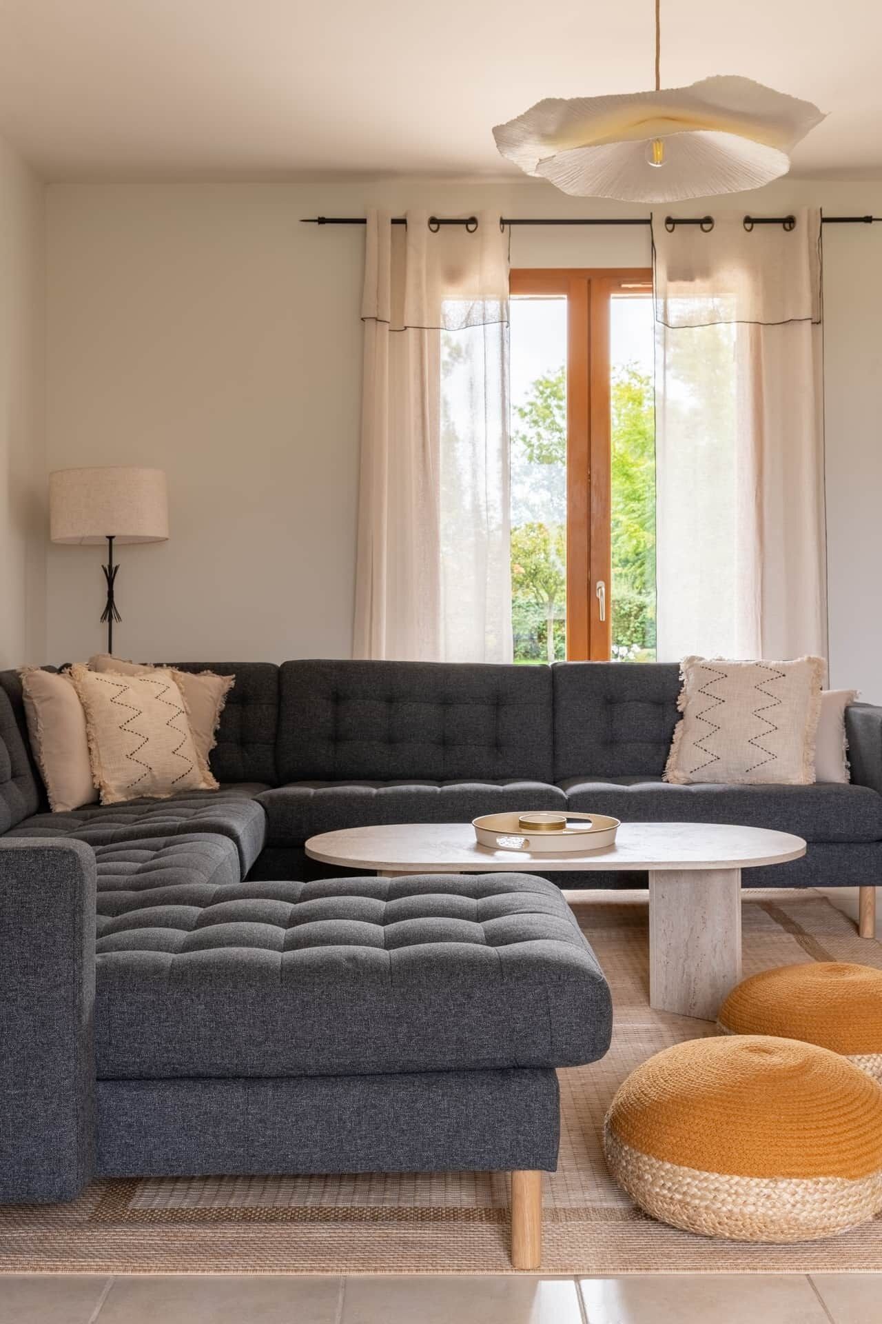 Un salon moderne avec un canapé d’angle, une table basse ronde et un luminaire suspendu.