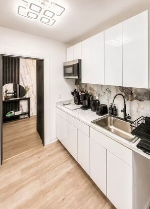 Cocina moderna con armarios blancos, un lavamanos de acero inoxidable y un microondas.