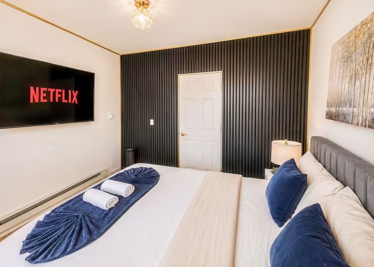 Una habitación de hotel con una cama, un televisor de pantalla plana montado en la pared, una puerta y una lámpara también fijada a la pared.