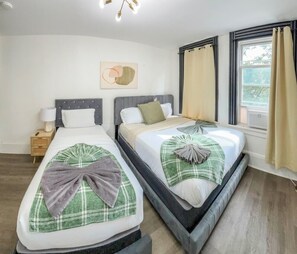 A hotel room with two beds, a bedside table with a lamp, a wall-mounted artwork, and a window with curtains. - 20 Minutes to Manhattan with a Full Kitchen (Apartment 5) (West New York)