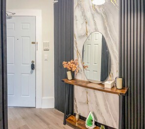 A hallway with a white door, a marble wall with a mirror, a wooden console table with decorative items, and a grey striped wall. - 20 minutes from Manhattan with a fully equipped kitchen (Apartment 5) (West New York)