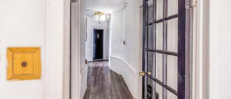 A hallway with a wooden floor, a door with glass panels, and a light fixture on the ceiling.