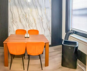 A room with a marble wall, a wooden table with four chairs, and a black trash bin. - 20 minutes from Manhattan with a fully equipped kitchen (Apartment 5) (West New York)