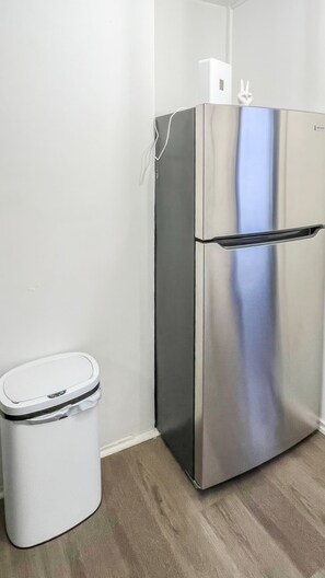 A stainless steel refrigerator and a white trash bin in a room with a light-colored floor. - 20 Minutes to Manhattan with a Full Kitchen (Apartment 5) (West New York)