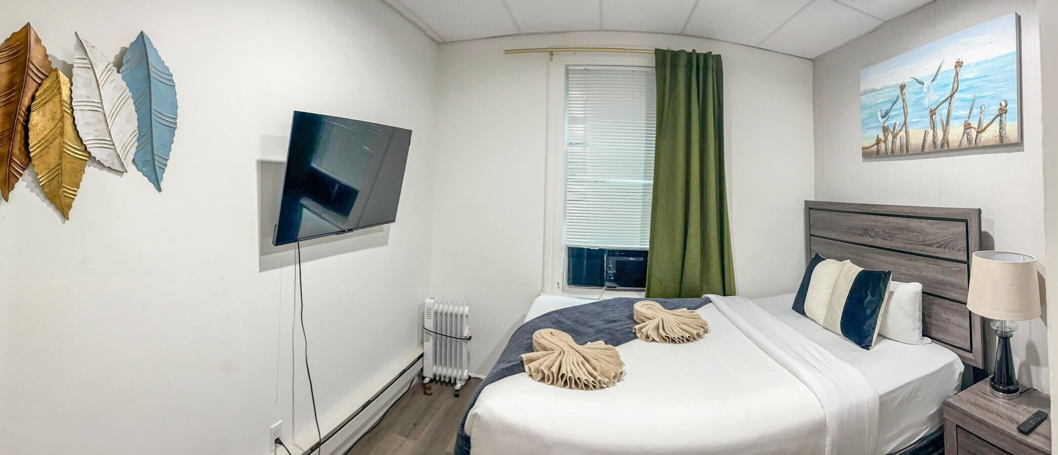Quarto de hotel com cama, televisão de tela plana, radiador, janela com cortinas e um quadro na parede.