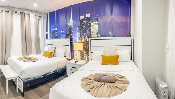 Een hotelkamer met twee bedden, een stadsgezicht muurschildering, een bankje en een nachtkastje met een lamp.