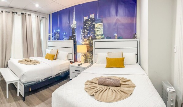 Ein Hotelzimmer mit zwei Betten, einer Stadtlandschaftsmalerei an der Wand, einer Bank und einem Nachttisch mit Lampe.