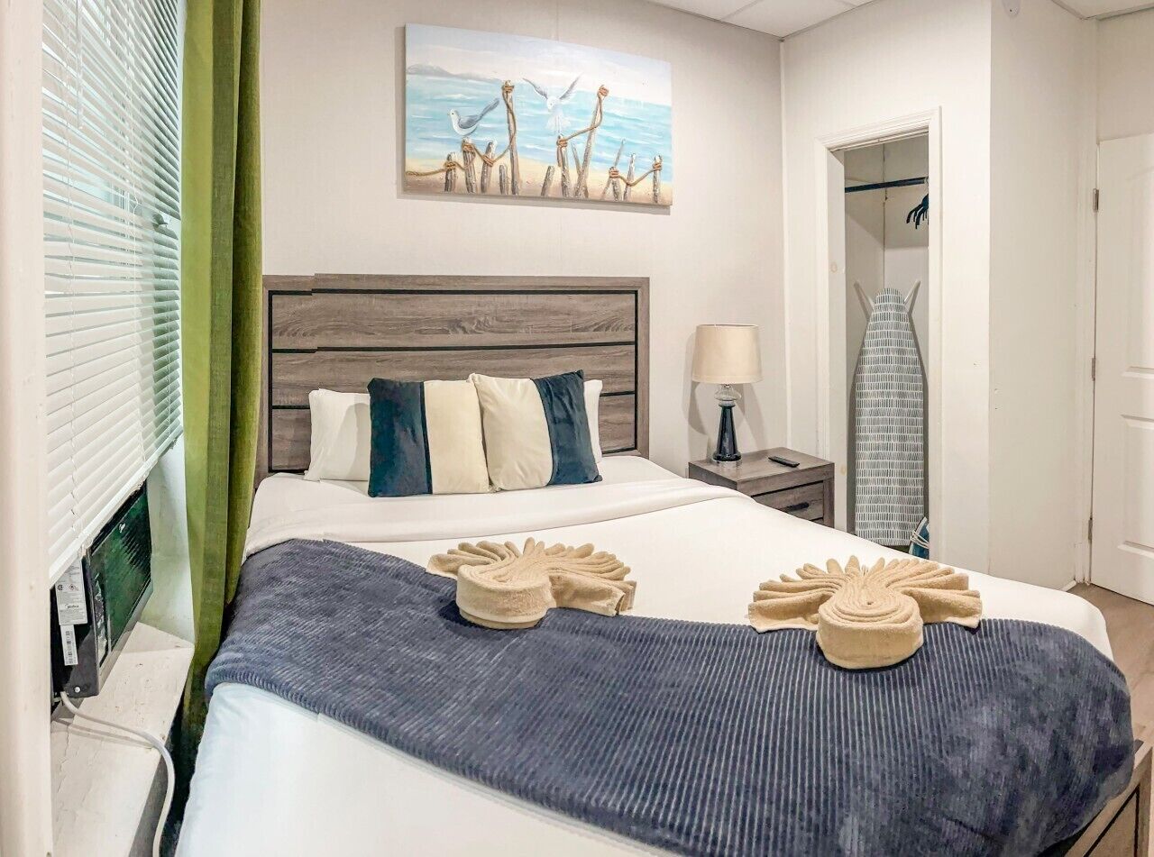 Ein Hotelzimmer mit einem Bett, einem Nachttisch, einer Lampe, einem Gemälde und einem Schrank mit einem Kleidungsstück.