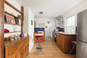 A kitchen with wooden cabinets, a stainless steel refrigerator, and a bar stool. - New! Cosy Hackney 3BR | 7 Mins to London Fields (Greater London)