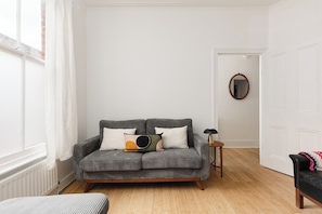 A living room with a grey sofa, a small side table, and a black chair. - New! Cosy Hackney 3BR | 7 Mins to London Fields (Greater London)