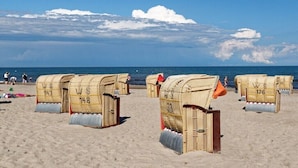 Strandhütten mit Nummern, an einem Sandstrand aufgereiht, mit dem Meer im Hintergrund.