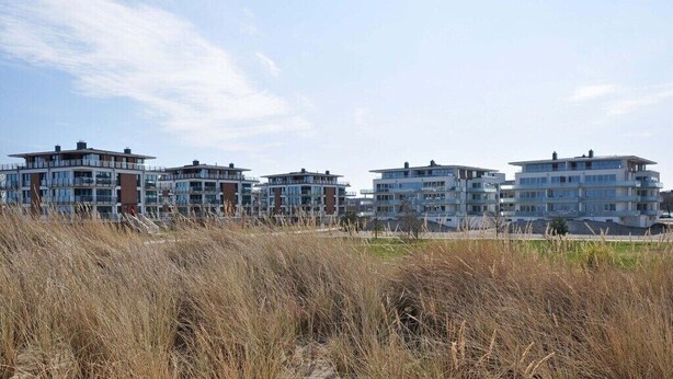 Eine Reihe moderner mehrstöckiger Gebäude mit flachem Dach, gelegen auf sandigem Gelände mit trockenem Gras im Vordergrund.