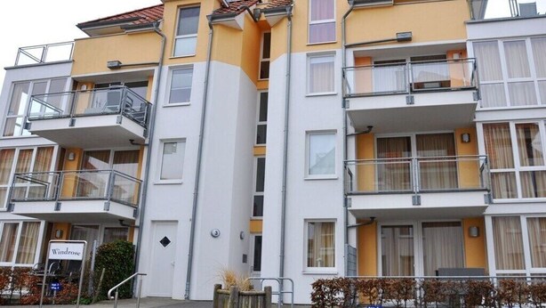 Un edificio residencial de varios pisos con balcones, una entrada visible y un letrero que indica el nombre 'Windrose'.