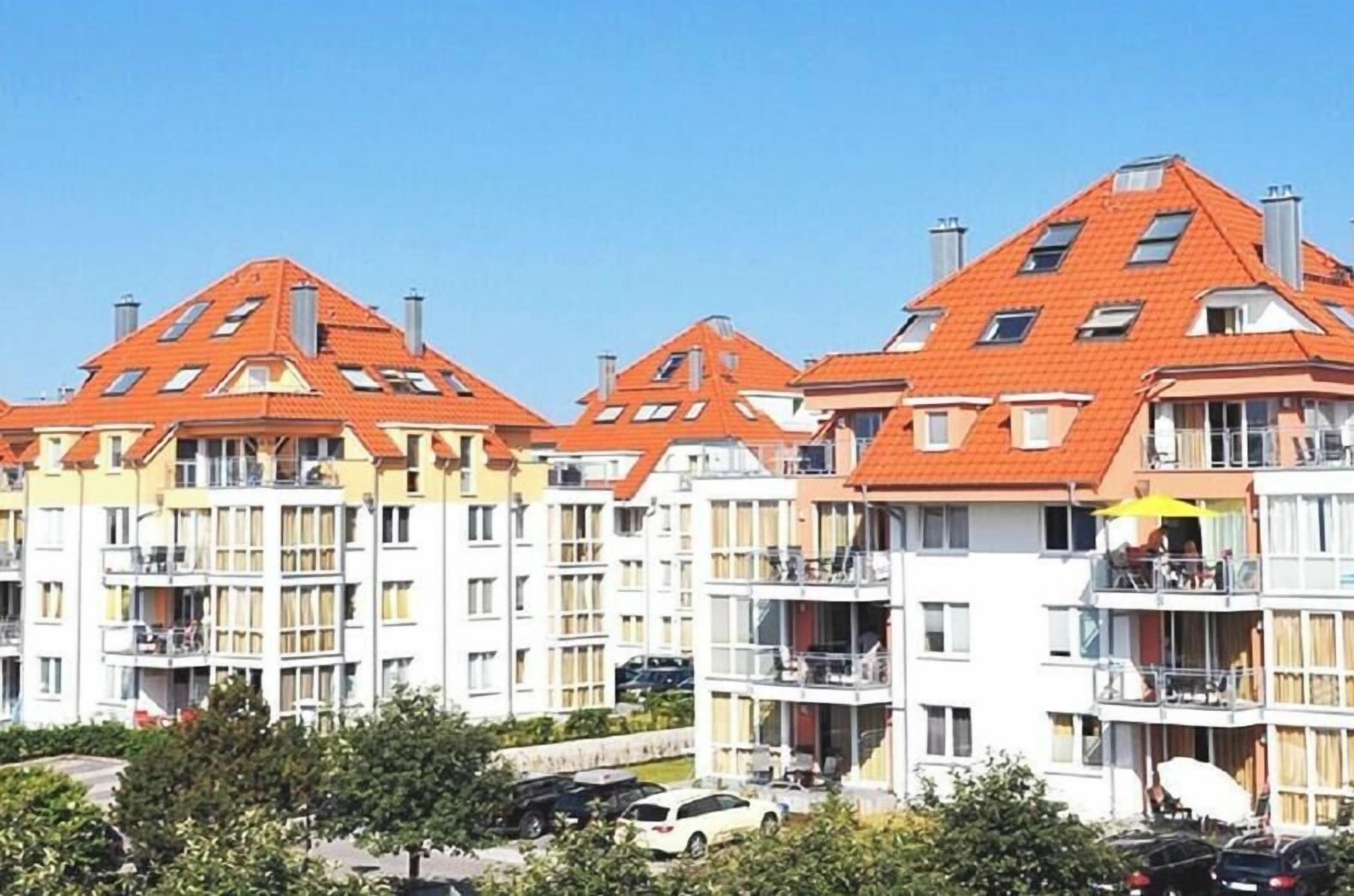 A multi-story residential building with a red-tiled roof, balconies, and a clear sky.