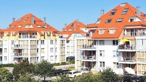 Un edificio residencial de varios pisos con techo de tejas rojas, balcones y cielo despejado.
