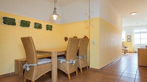 Un comedor con mesa de madera y sillas de mimbre, una lámpara colgante y piso de baldosas.