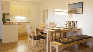 Una cocina compacta con microondas, lavamanos y cafetera. Hay una mesa de comedor con sillas y un banco.